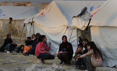 Displaced Syrians wait outside tents.