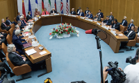 U.S. and Iranian negotiators sit around a cured table as media with cameras and microphones crowd the foreground.