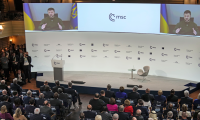 A wide shot of a crowd watching two large video screen with Ukraine President Zelenskyy on them at the Munich Security Conference