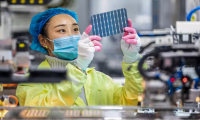 A piece of solar panel being inspected by someone in PPE.