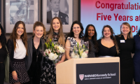 Women line up in front of a screen reading "congratulations on five years at HKS"